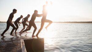 People jumping off a Pier into the sea with wet suits on